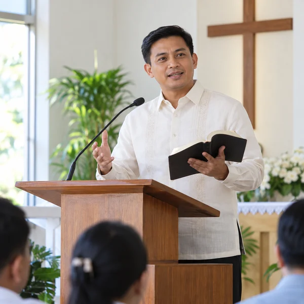 Pastor holding an open Bible while speaking from a lectern